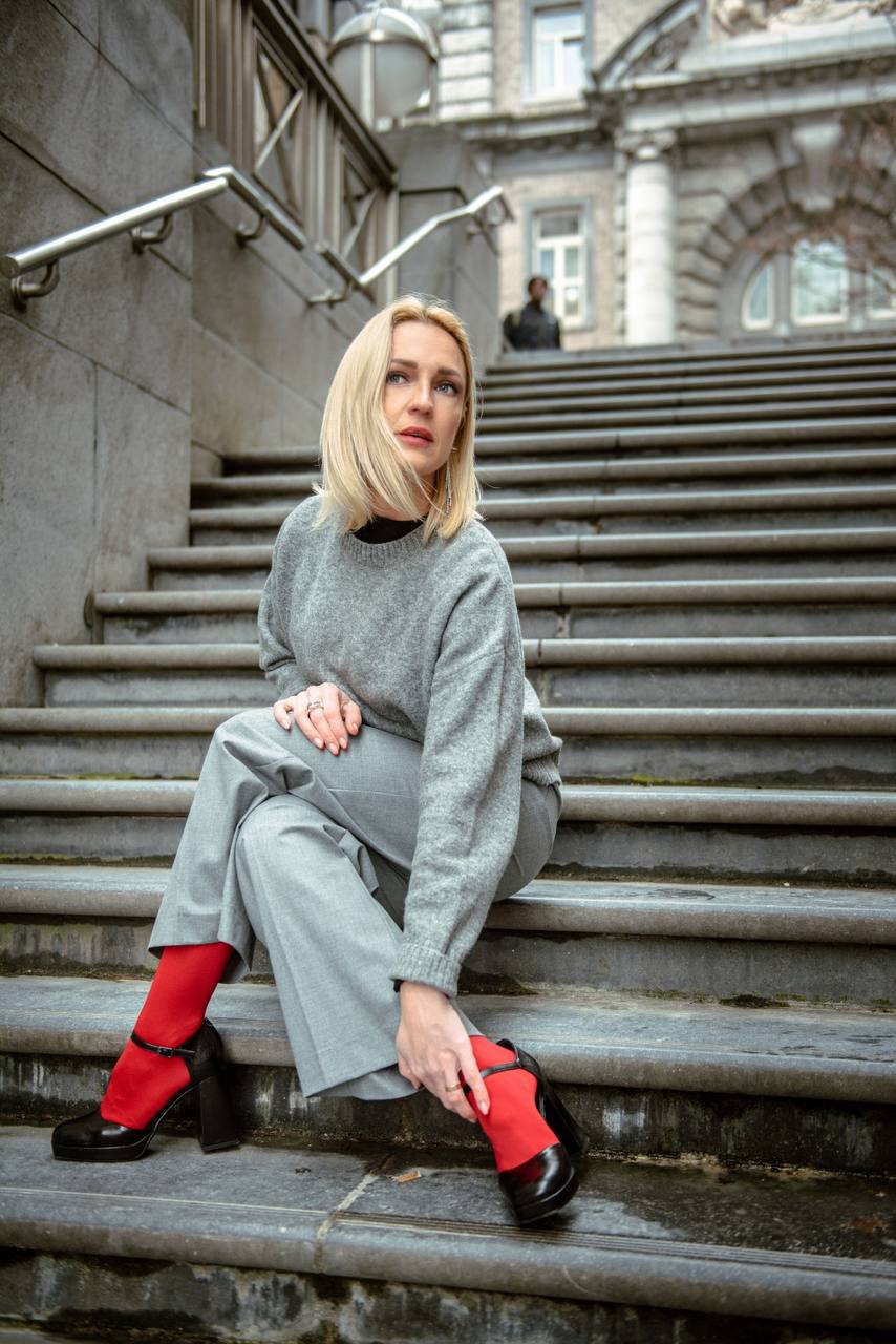 Portrait d'Alexandra en pull gris, dans un escalier en pierre